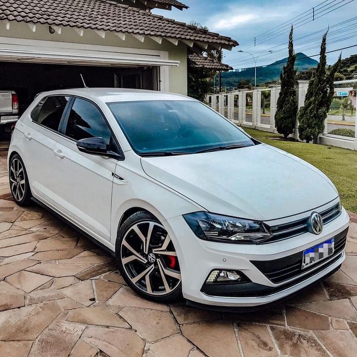 a white volkswagen car parked in front of a house with an open garage door on the side