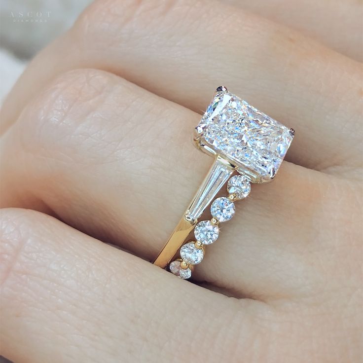 a woman's hand holding an engagement ring with three stones on the band and a diamond in the middle