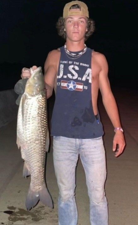 a man holding a fish in his right hand while standing on the beach at night