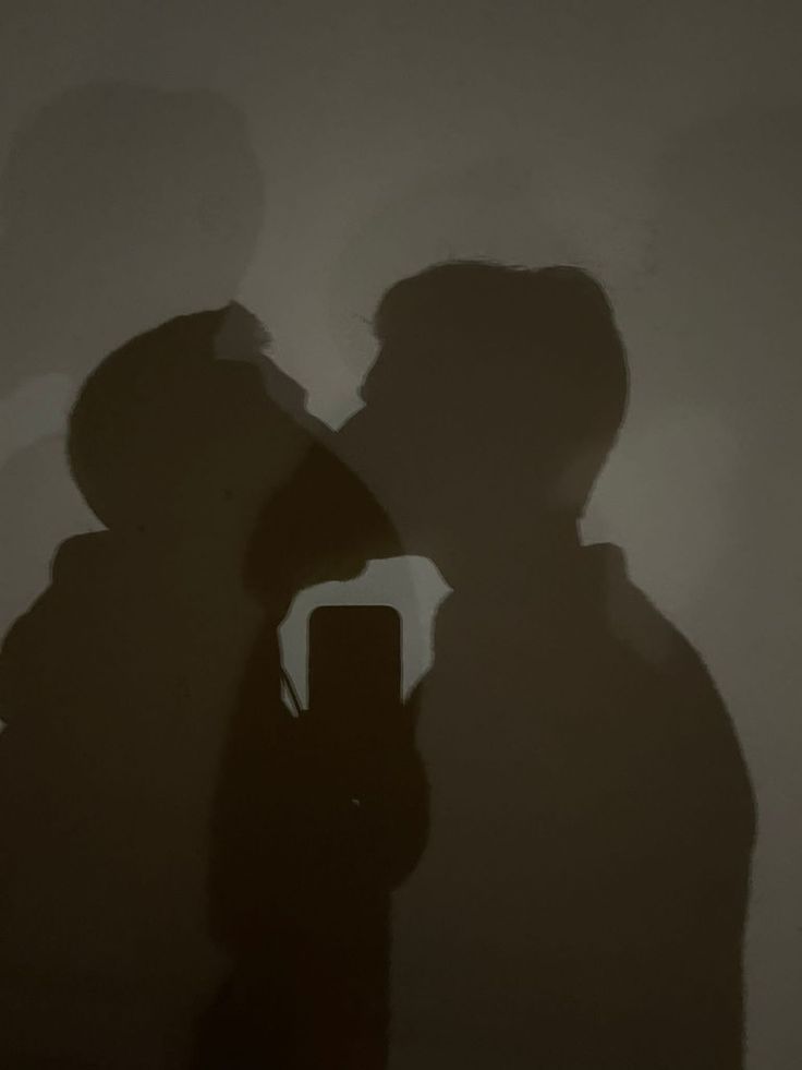 the shadow of two people standing in front of a wall with a cell phone on it