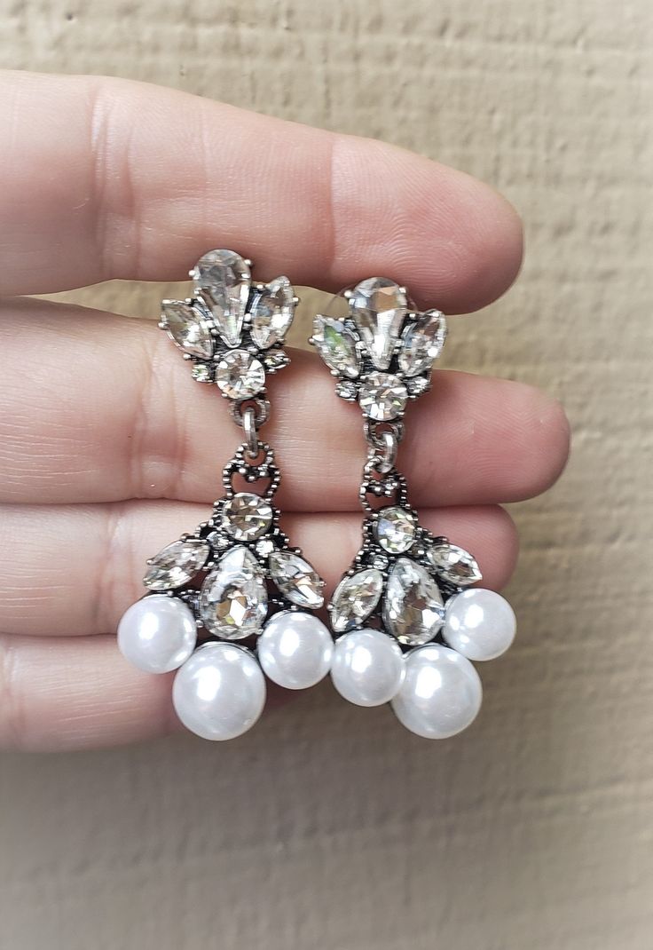 Elegant Vintage style Bridal Earrings. Made with clear crystals and crystal white pearls. They are about 2 inches long. Sparkling deco drama that makes a statement for brides or black tie affairs. Three large crystal white pearls followed by three clear AAA grade crystals, finished with the same crystals on the lobe. The metal is antique finish silver which makes the crystal pop out more. If you have any questions feel free to contact me via Etsy convo. Happy shopping with Simply Chic. Pearl Drop Dangle Crystal Earrings, Party Pearl Drop Crystal Earrings, Glamorous White Drop Chandelier Earrings, Party Pearl Teardrop Crystal Earrings, Pearl Teardrop Crystal Earrings For Party, Party Teardrop Pearl Crystal Earrings, White Crystal Pearl Drop Earrings, Party Crystal Earrings With Pearl Drop, White Pearl Drop Crystal Earrings