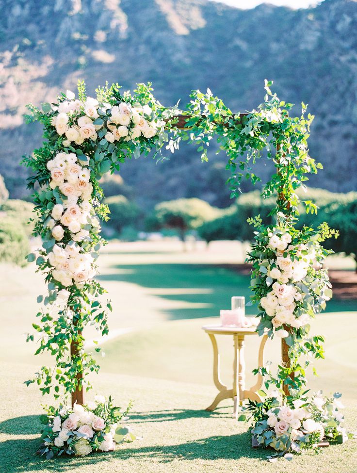 an outdoor ceremony setup with white flowers and greenery on the arch, overlooking a golf course