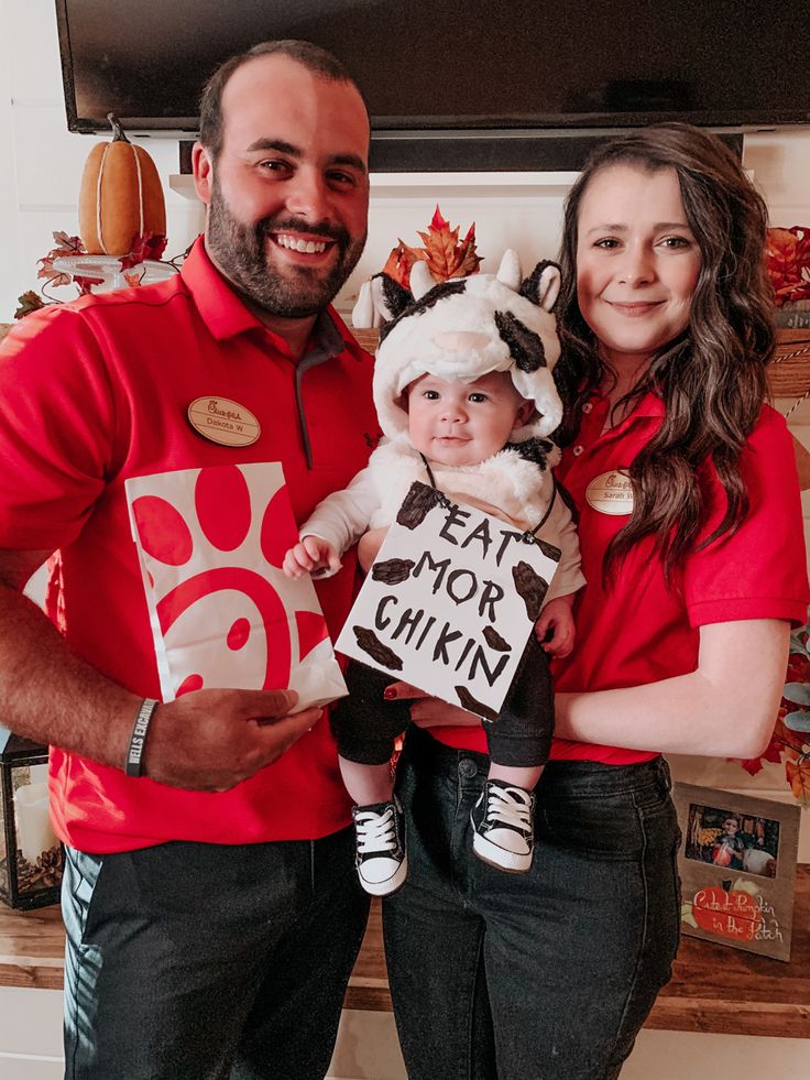 a man and woman holding a baby dressed up as a cow with a sign that says eat more chicken