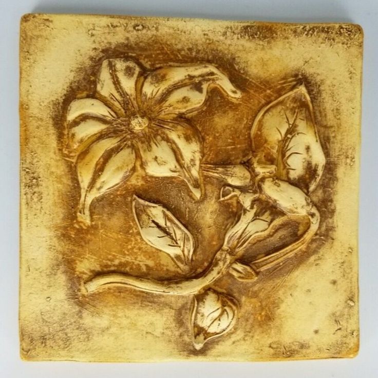 a ceramic tile with flowers and leaves on it's side, in gold color