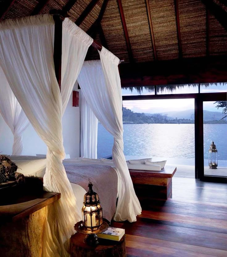 a bed with white sheets and pillows in front of a large body of water that has boats on it