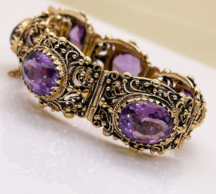 "GORGEOUS VINTAGE 14K AMETHYST  LINK BRACELET This bracelet is stunning!  Likely Circa 1940's but it could be older. 14K Yellow Gold Featuring 48.48 Carats of Faceted Oval Amethysts Push Clasp & Safety Chain Closures Marks: 14K and a Hallmark of the Goldsmith  Weight (g): 71.3 Clasp Style: Push Clasp, Safety Chain Carat Total Weight: 48.48 Stone Count: 6 Stone Shape: Faceted, Oval Color: Purple Saturation: Strong Type/Clarity: Eye Clean Transparency: Transparent Condition: Very Good Vintage Cond Antique Yellow Gold Bracelets For Evening, Antique Yellow Gold Bracelet For Evening Wear, Antique Gemstone Bracelet For Anniversary, Estate Style Oval Gold Jewelry, Antique Yellow Gold Bracelet For Formal Occasions, Antique Yellow Gold Bracelets For Formal Occasions, Vintage Gold Bracelet With Intricate Design, Antique Gemstone Bracelets For Formal Occasions, Vintage Gemstone Bracelet For Formal Occasions