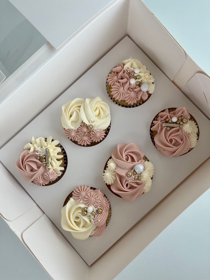 six cupcakes in a box with pink and white frosting on the top