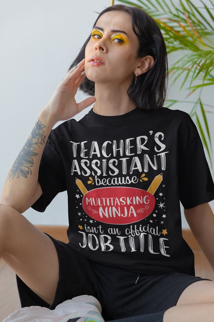 a woman sitting on the floor wearing a teacher's assistant t - shirt and yellow eyeshadow