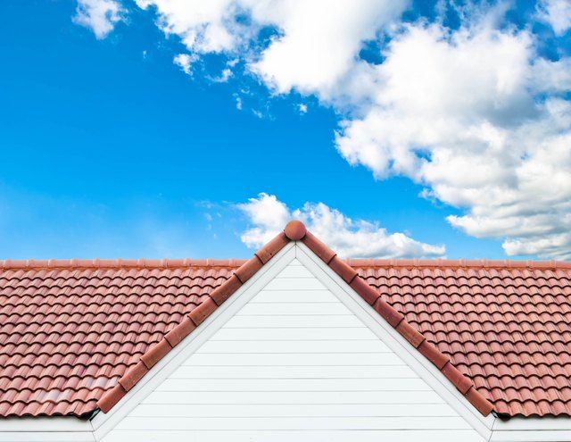 the roof of a white house with red tile on it and blue sky in the background