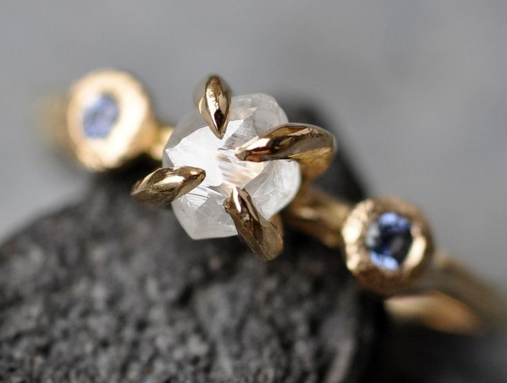 two gold rings with white and blue stones on top of each other, sitting on a rock