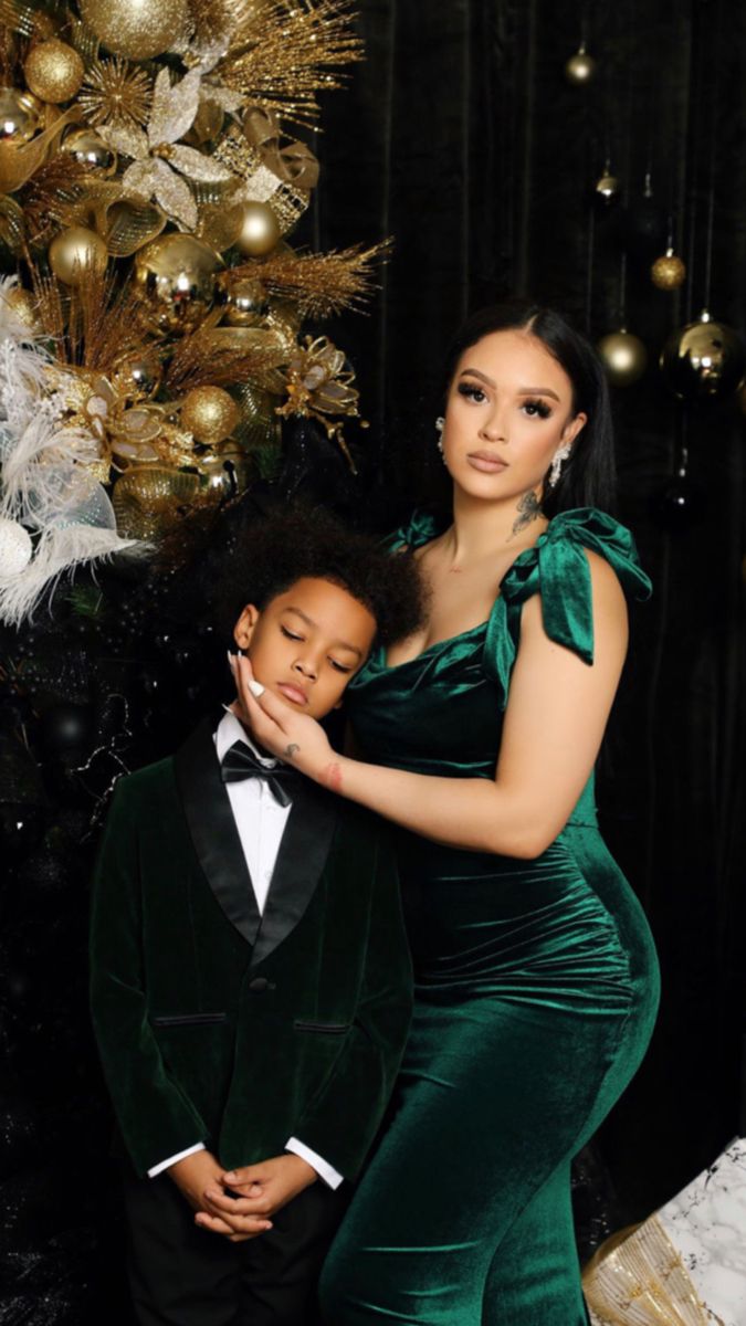 a woman in a green dress standing next to a little boy wearing a tuxedo