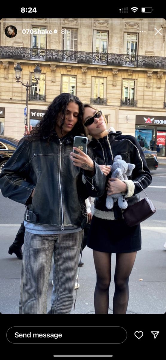 two women standing next to each other in front of a building and one holding a cell phone