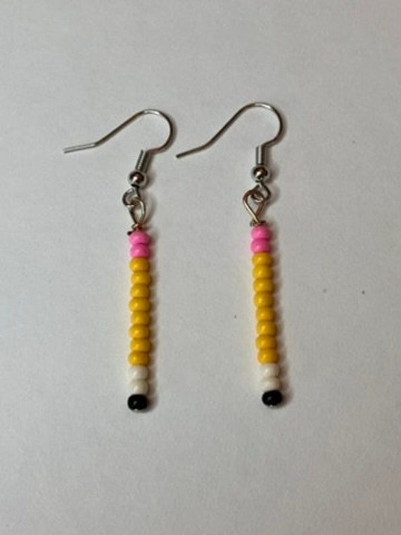 two yellow and pink beads are hanging from silver earwires on a white surface