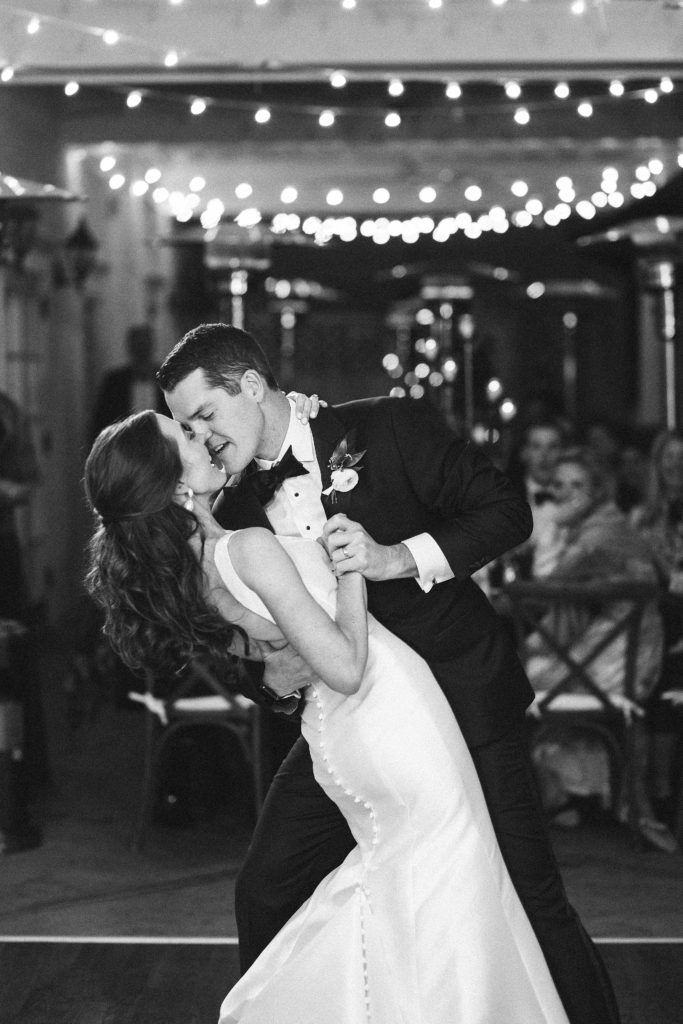 a bride and groom dance at their wedding reception in black and white with string lights