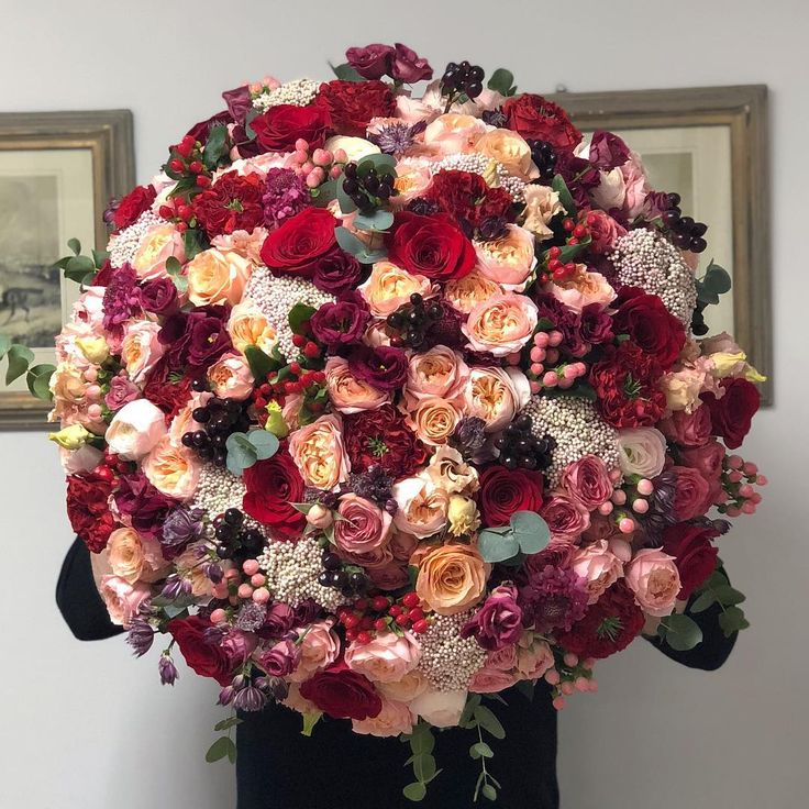 a woman holding a large bouquet of red and pink flowers in her hands with two framed pictures on the wall behind her