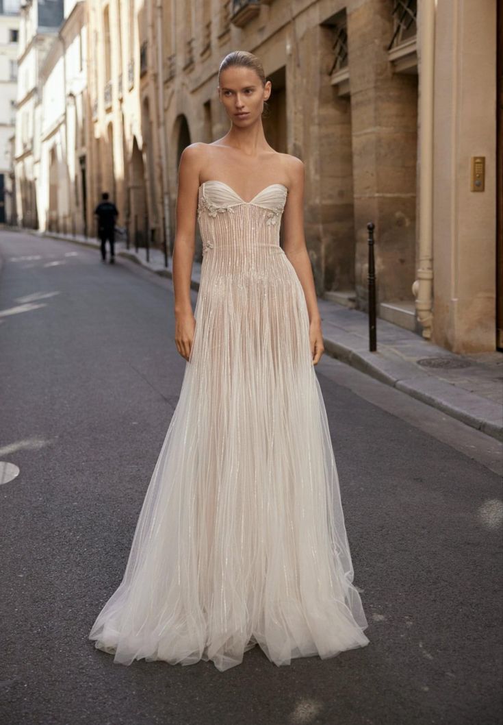 a woman is standing in the middle of an empty street wearing a wedding dress with pleated skirt