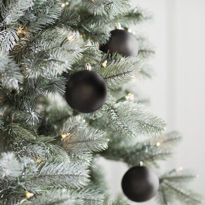 a christmas tree with black ornaments hanging from it's branches in front of a white wall