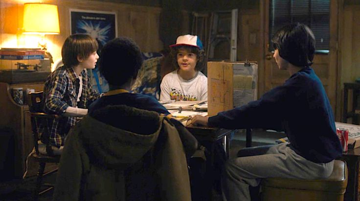 three people sitting at a table in a dark room with a lamp on the wall