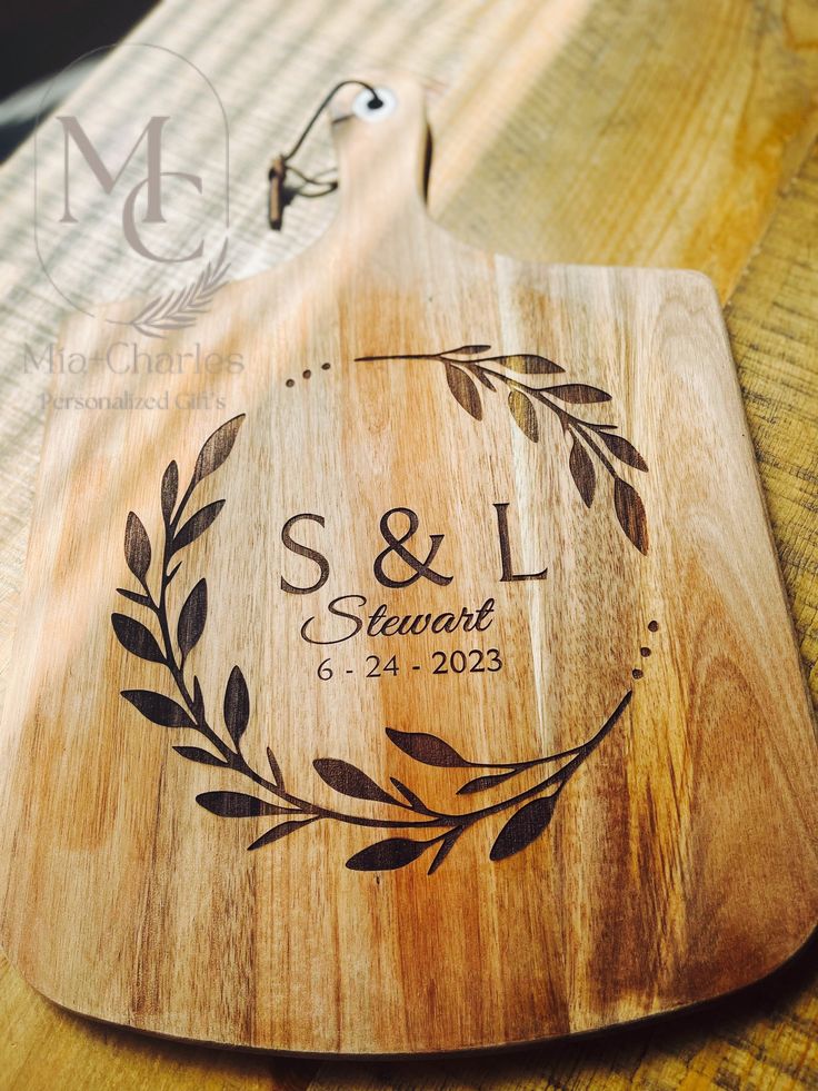 a wooden cutting board with a couple's initials on it and an olive wreath