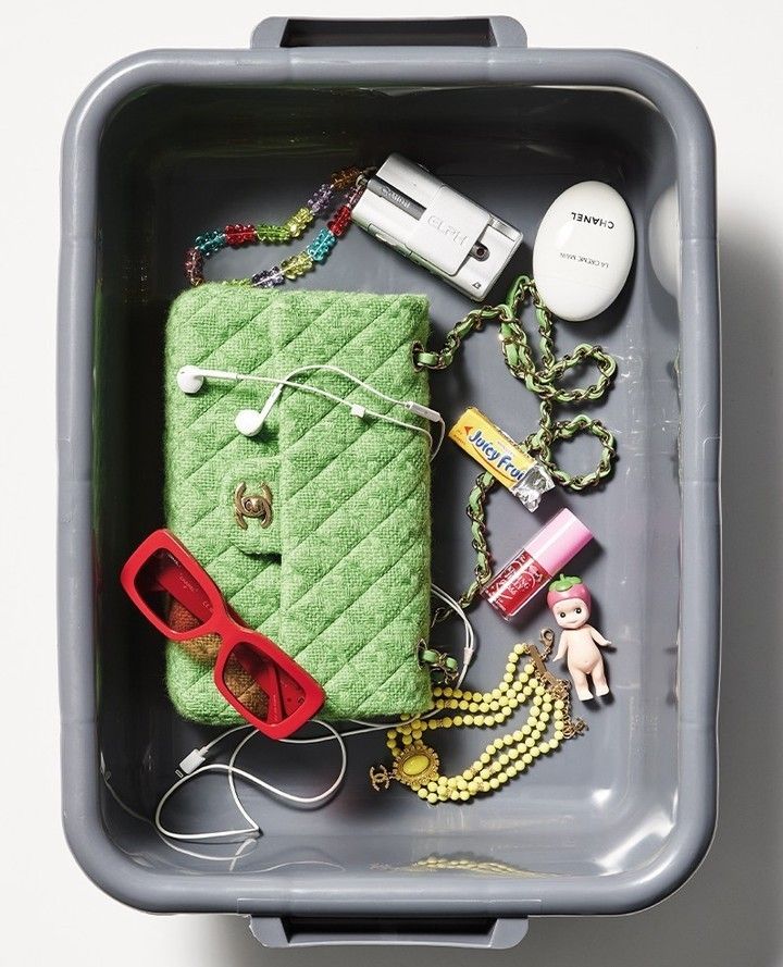 the contents of a green purse are in a gray container with sunglasses and other items