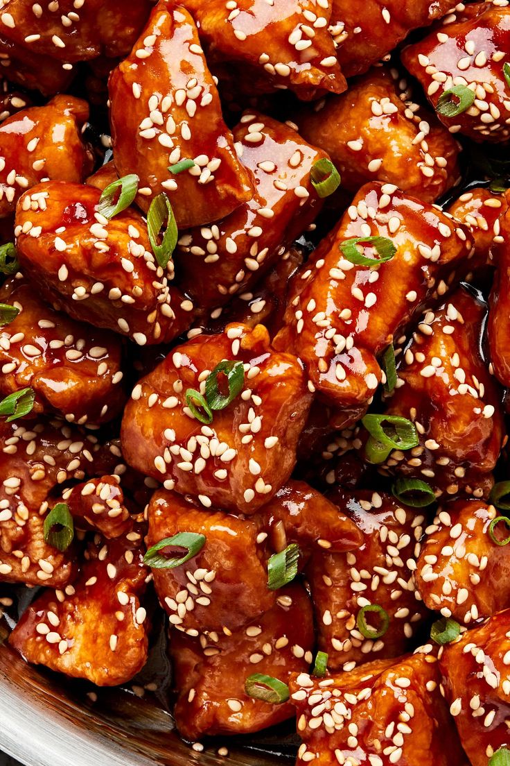 sesame seed chicken in a bowl with sauce and green garnish on the side