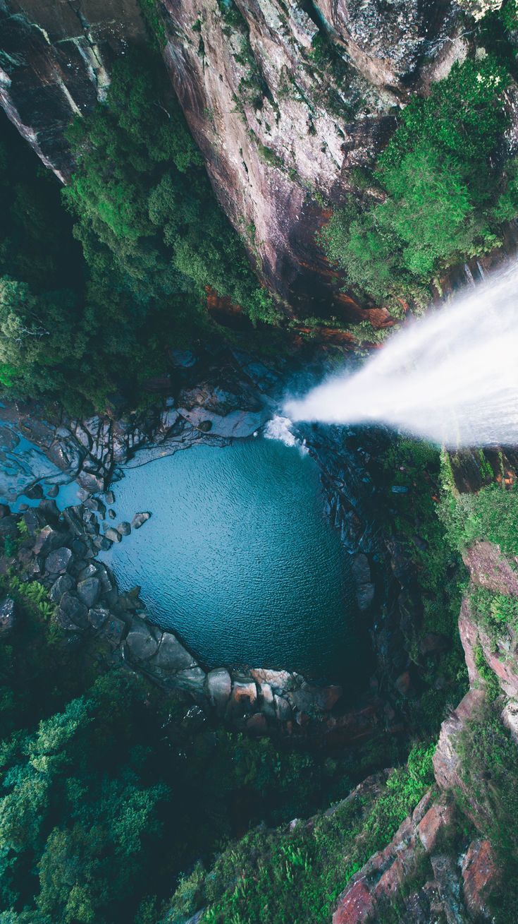 an aerial view of a lake surrounded by rocks and trees with a jet spraying water on it