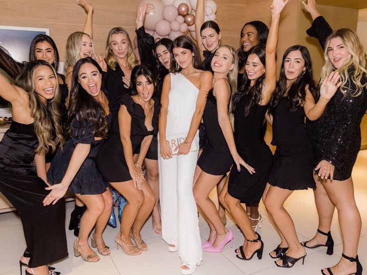 a group of women in black dresses posing for a photo with one woman holding up a balloon