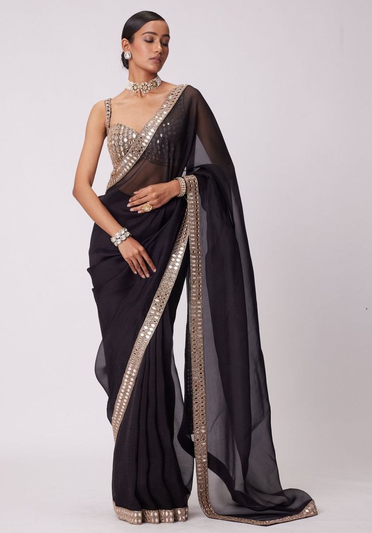 Elevate your style with black saree, crafted in luxurious organza. The saree features an exquisite hand embroidered mirror border adorned with rose gold embroidery. Paired with a svelte sleeveless blouse that adds a modern touch. Perfect for cocktail parties, this saree set will make you the center of attention. Composition : Saree - Organza & Blouse - Georgette Care: Dry Clean Only and Vacuum Storage This product can be customized for sleeves, length and colour Delivery : 6-8 weeks as the product is hand crafted. Check Size Guide or choose MySize for free customisation (All Sizes above XL can be made at 15% additional cost) For more information and sizes please contact fabiliciousfashion@gmail.com or visit our Copenhagen studio. About the Designer : Introducing Vvani by Vani Vats, the ult Black Organza Saree, Mirror Blouse, Fashion Course, Mirror Embroidery, Organza Blouse, Female Dress, Indian Wedding Wear, Saree Blouses, Black Saree