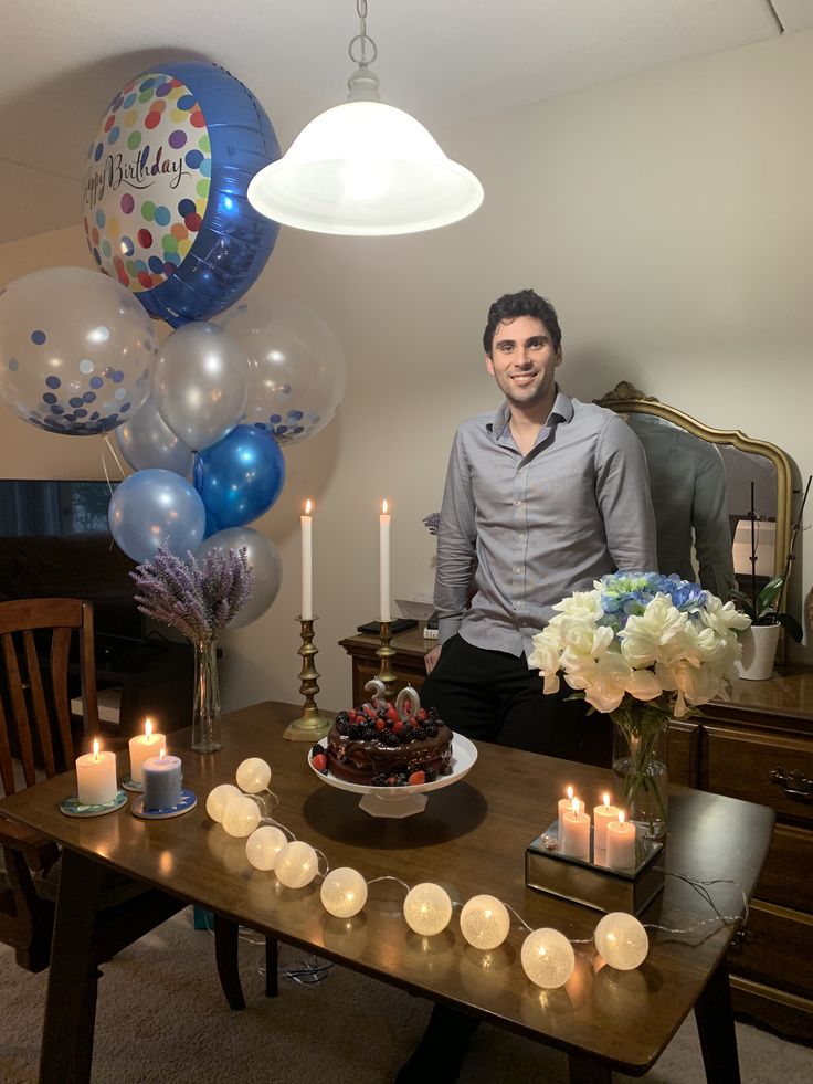 a man sitting in front of a cake with candles on it and balloons behind him