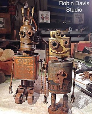 two rusty robot statues sitting on top of a table next to each other in front of a pile of tools