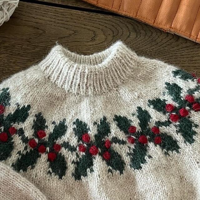 a white sweater with red and green flowers on it sitting on top of a wooden floor