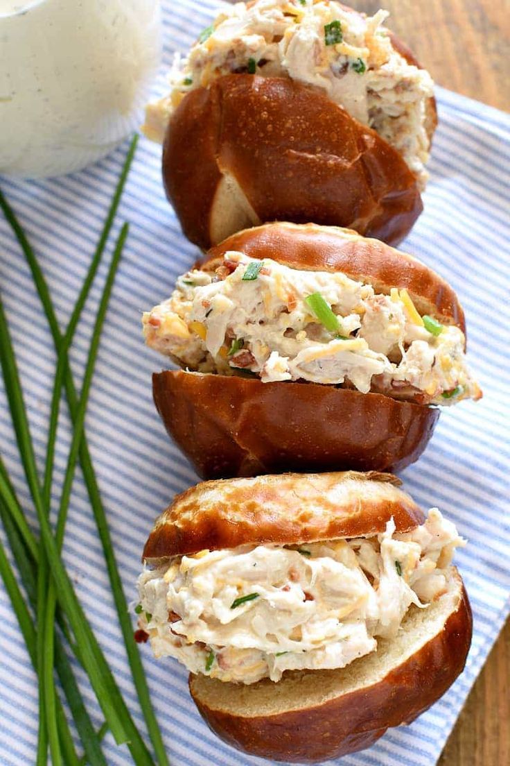 three bagels filled with chicken salad on top of a blue and white striped napkin