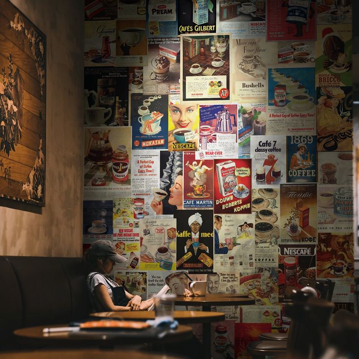 a woman sitting at a table in front of a wall covered with posters