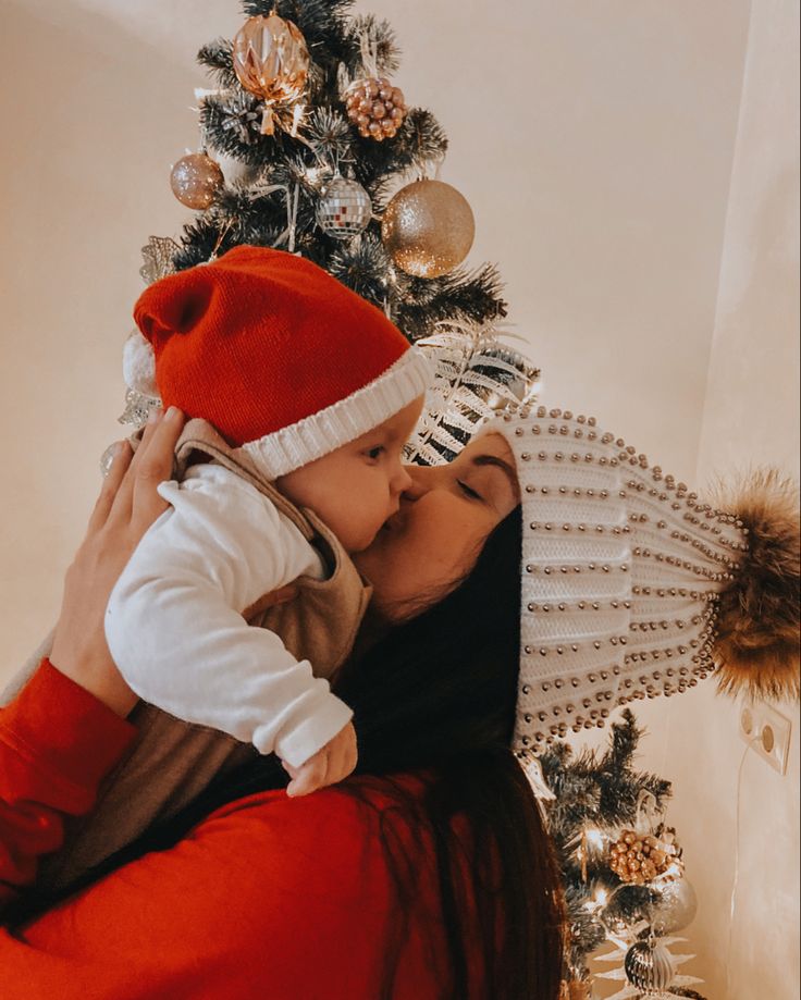 a woman holding a baby in front of a christmas tree with ornaments on the top