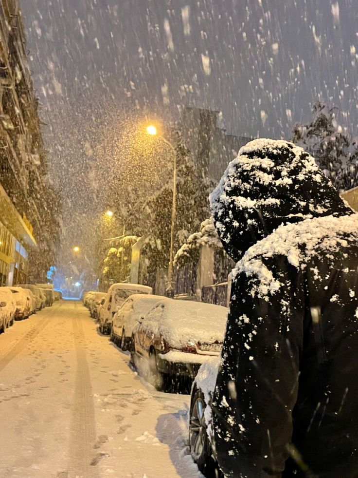 a person standing on the side of a snowy street next to parked cars and buildings