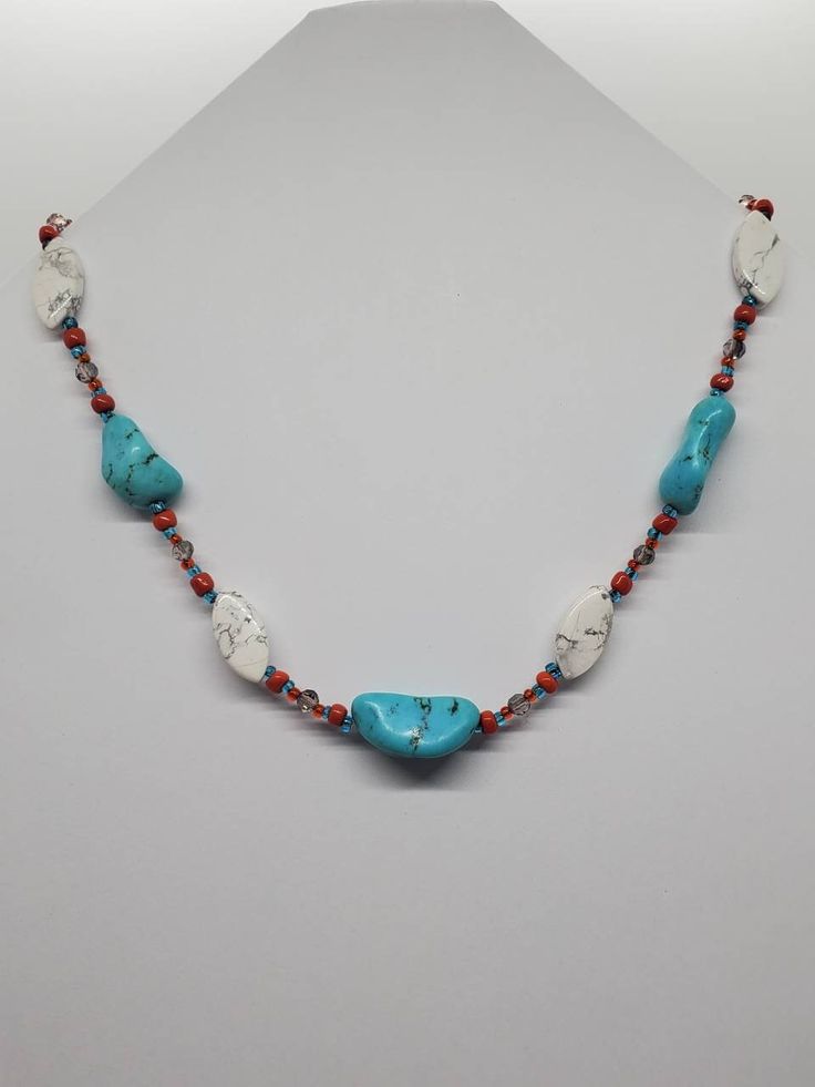 This one of a kind necklace consists of unusual, almond shaped  howlite beads and turquoise-dyed howlite nugget beads. It is accented by orange glass beads and turquoise colored seed beads and smokey, faceted, round beads. It has a large, gold tone lobster clasp and comes  in a matching organza pouch. Bohemian Turquoise Howlite Beaded Necklace, White Bohemian Turquoise Necklace As Gift, Bohemian White Turquoise Necklace As Gift, Bohemian Howlite Beaded Necklace With Gemstone Beads, Bohemian Howlite Gemstone Beaded Necklaces, Bohemian Beaded Howlite Necklaces, Handmade Adjustable White Turquoise Necklace, Turquoise Howlite Necklace With Natural Stones, Bohemian Style Turquoise Gemstone Beads Necklace