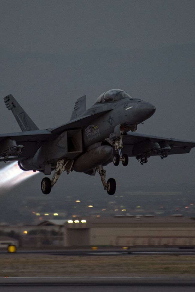 a fighter jet taking off from an airport runway at night with the landing gear down