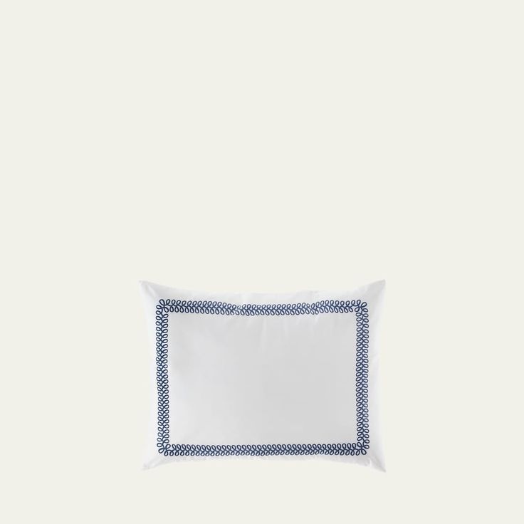 a white pillow with blue and white trim on the front, sitting against a white wall