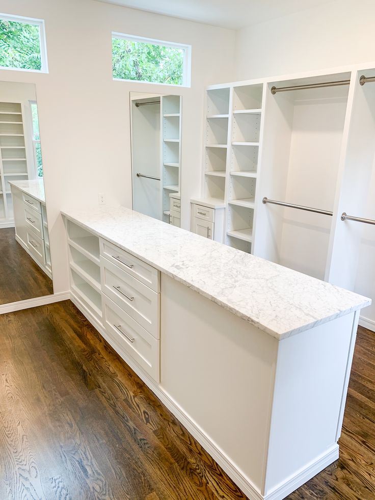 an empty kitchen with white cabinets and marble counter tops, along with hardwood floors in the middle