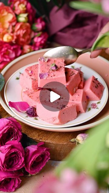 a white plate topped with pieces of cake next to pink flowers and a silver spoon