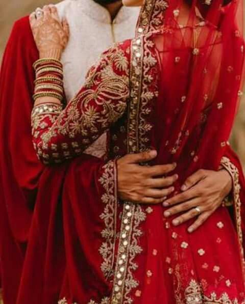 a woman in a red and gold bridal outfit hugging her husband on the forehead