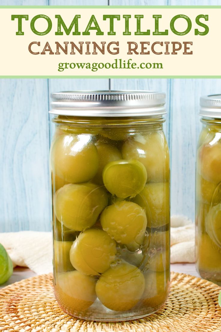 two jars filled with green olives sitting on top of a table