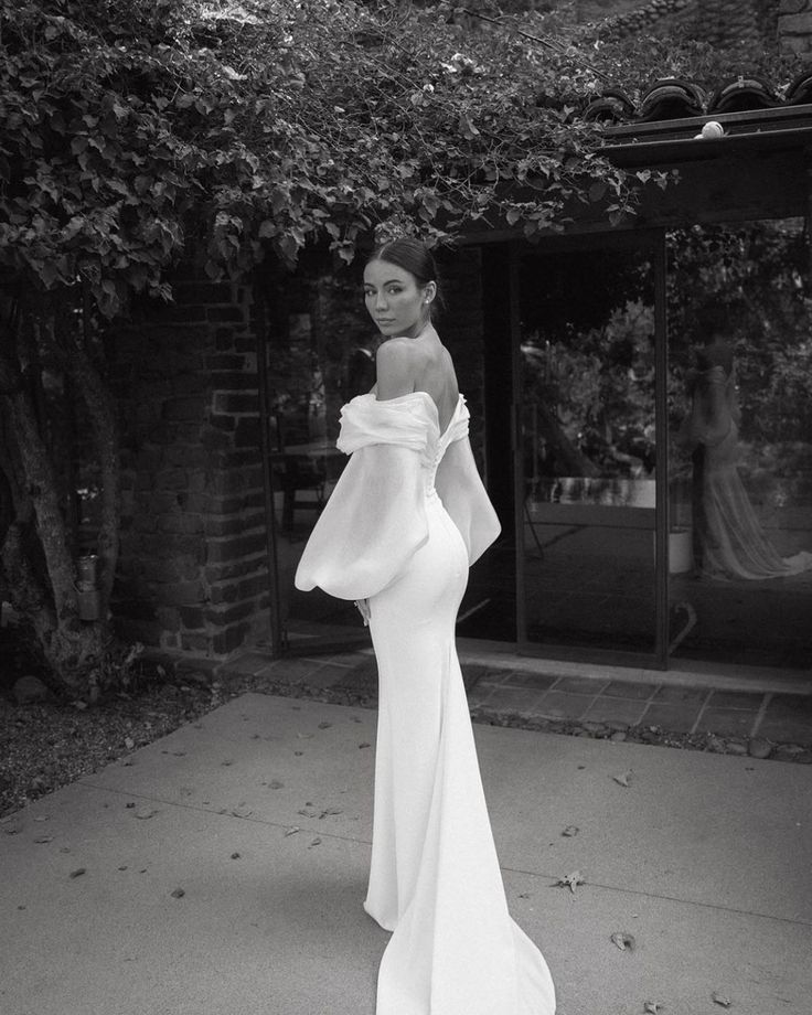 a woman in a white dress is standing on the sidewalk with her arms behind her back