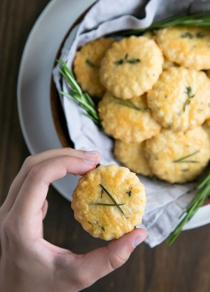 a person holding up a small biscuit in front of a bowl of rosemary sprigs