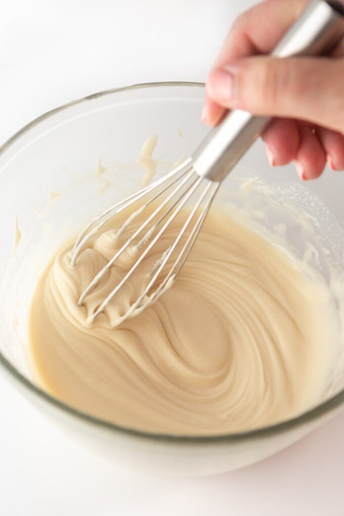 a whisk being mixed in a glass bowl with white batter on the side