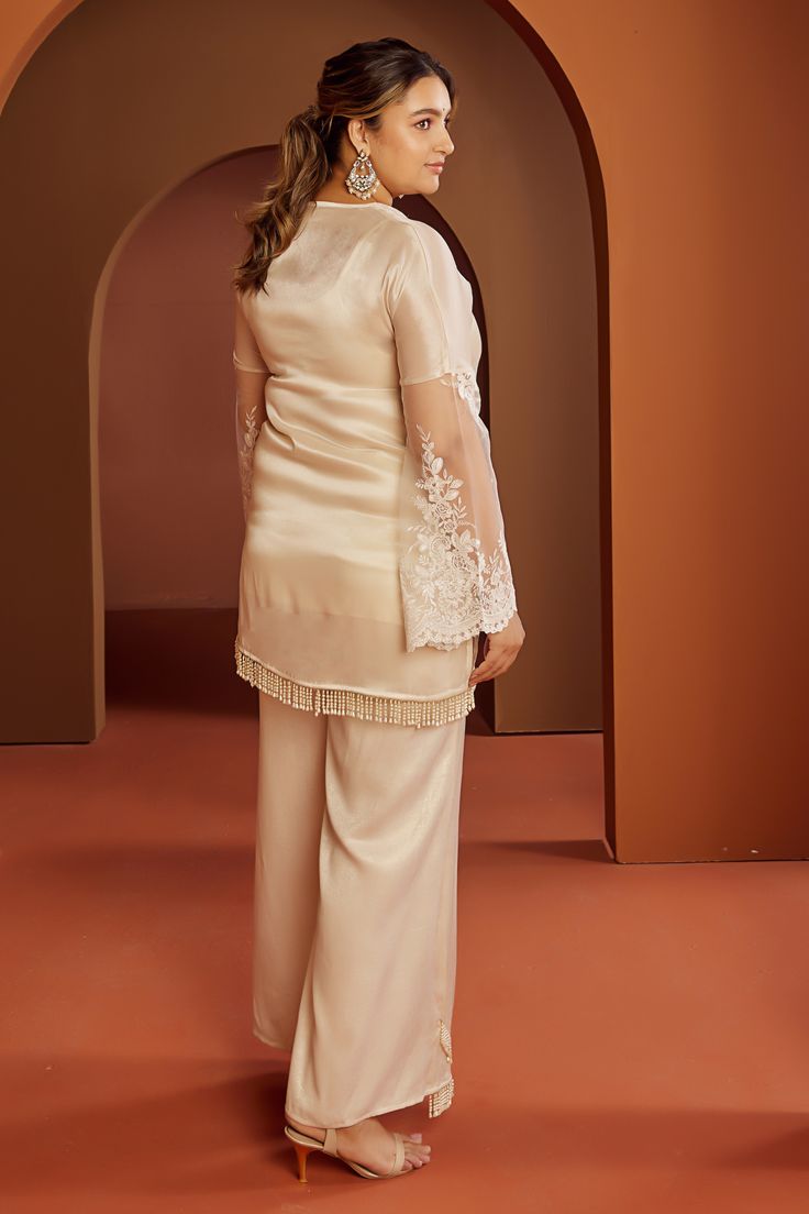 Ivory kurta with a V-neckline, embroidered net fabric insert on the sides and pearl latkans at the hemline,. Paired with a pant, matching organza dupatta and slip.
Components: 4
Pattern: Embroidered
Type Of Work: Hand embroidered
Neckline: V Neck
Sleeve Type: Bell
Fabric: Organza, Satin, Net
Color: Ivory
Other Details: 
Approx. product weight: 0.5 kg
Model height: 5ft 9inches, wearing size 2XL
Occasion: Mehendi and Haldi - Aza Fashions Elegant V-neck Sets For Wedding Night, Eid Wedding V-neck Palazzo Set, V-neck Resham Embroidery Palazzo Set For Wedding, Elegant Cream Palazzo Set For Eid, Elegant Embroidered V-neck Palazzo Set, Festive V-neck Elegant Palazzo Set, Elegant V-neck Wedding Kurta, Elegant V-neck Palazzo Set With Resham Embroidery, Elegant Sets With Resham Embroidery And V-neck