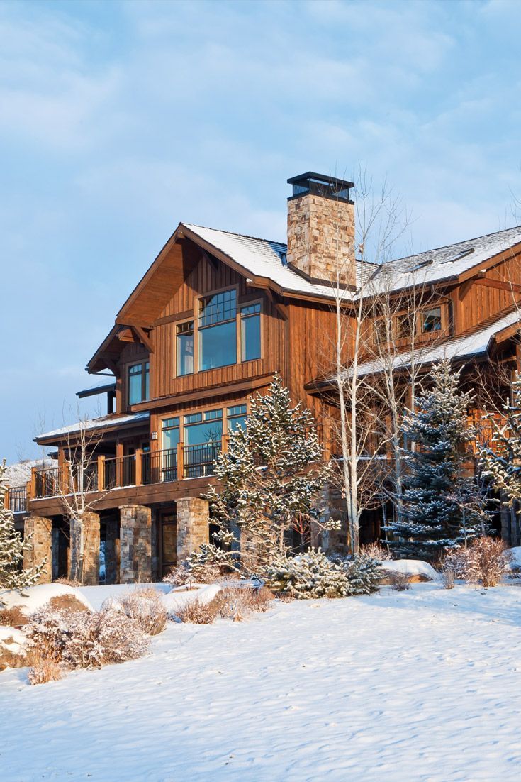 a large wooden house with snow on the ground and trees around it in front of a blue sky