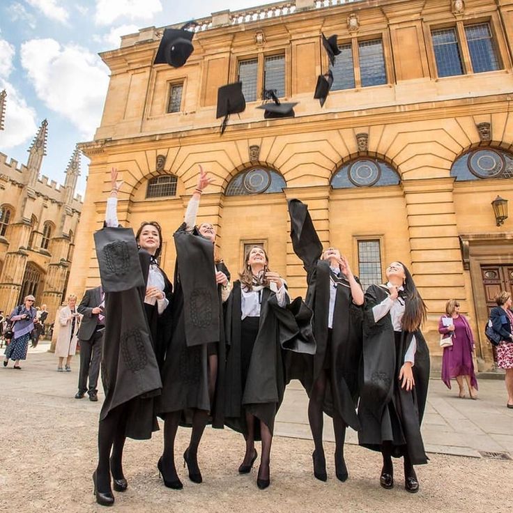 three graduates throwing their caps in the air outside an old building with people walking around