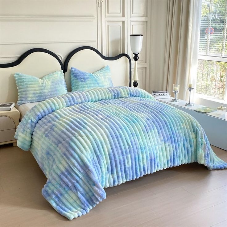 a bed covered in blue and green comforter next to a window