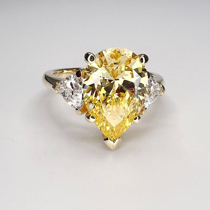 "This ring is a pear shape canary yellow simulated diamond with trillion accents made with solid 14k white gold item #5402 -Approximate total carat weight:  4.80ctw diamond equivalent  -Center Stone Size: 13x9mm  approx. 4.00ct diamond equivalent -Gem Type:  simulated diamond -Stone Shape:  pear shape  -Stone Clarity: VVS1 -Stone Color: canary yellow -Moh's Scale:  8.5 Hardness -Accent Stones: 2 trillions  -Stone size: 5x5mm approx 0.40ct each diamond equivalent -Gem Type:  simulated diamond -Me Yellow Pear Diamond Engagement Ring, Oval Yellow Diamond Promise Ring, Yellow Diamond Solitaire Jewelry, Yellow Solitaire Diamond Jewelry, Yellow Diamond Rings With Accent Stones, Elegant Yellow Pear-shaped Diamond Ring, Pear-shaped Yellow Jewelry With Diamond Accents, Yellow Rings With Diamond Accents For Promise, Yellow Pear-shaped Jewelry With Diamond Accents